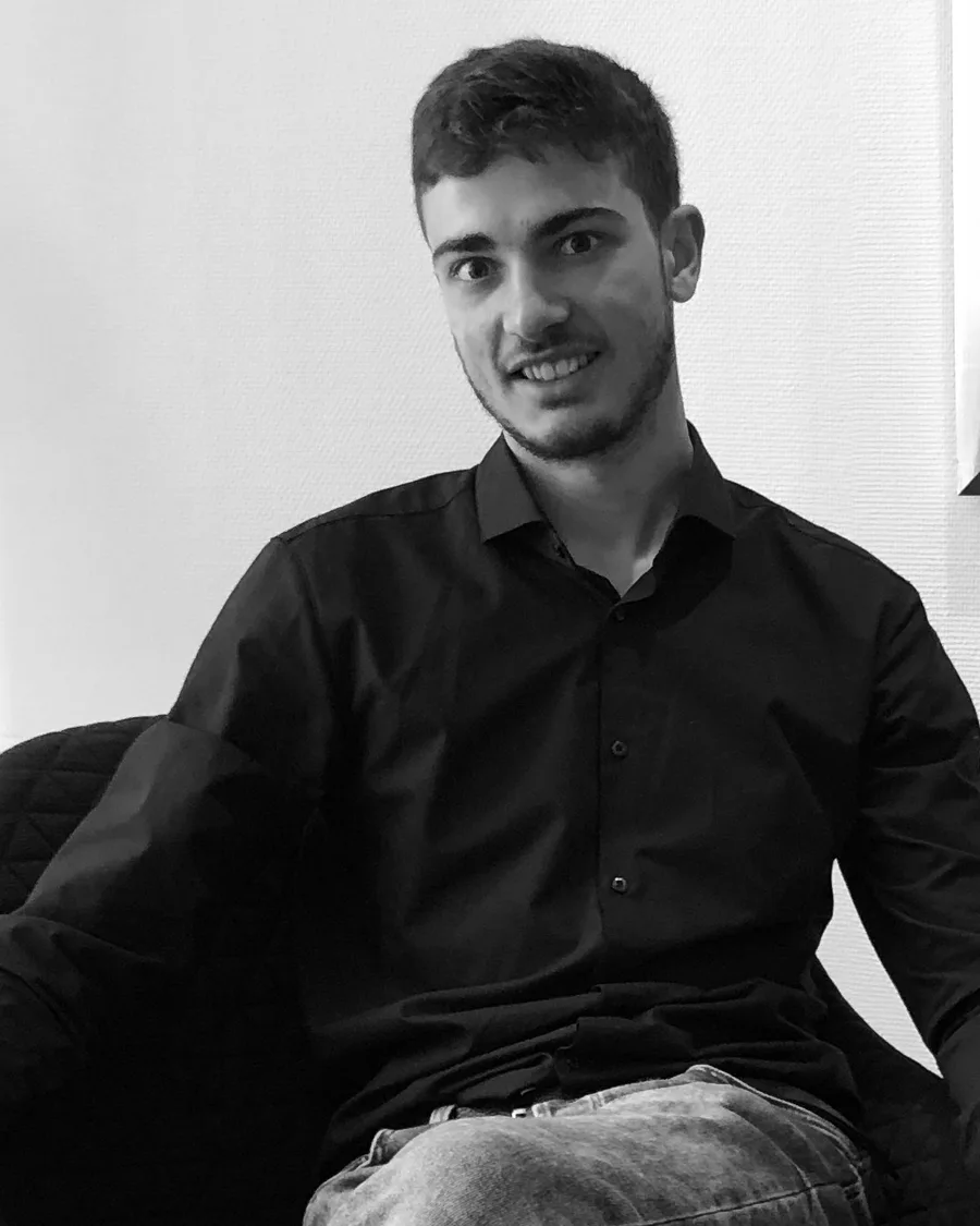 Sayid Bilal seated in a dark armchair in a navy shirt, smiling to camera.